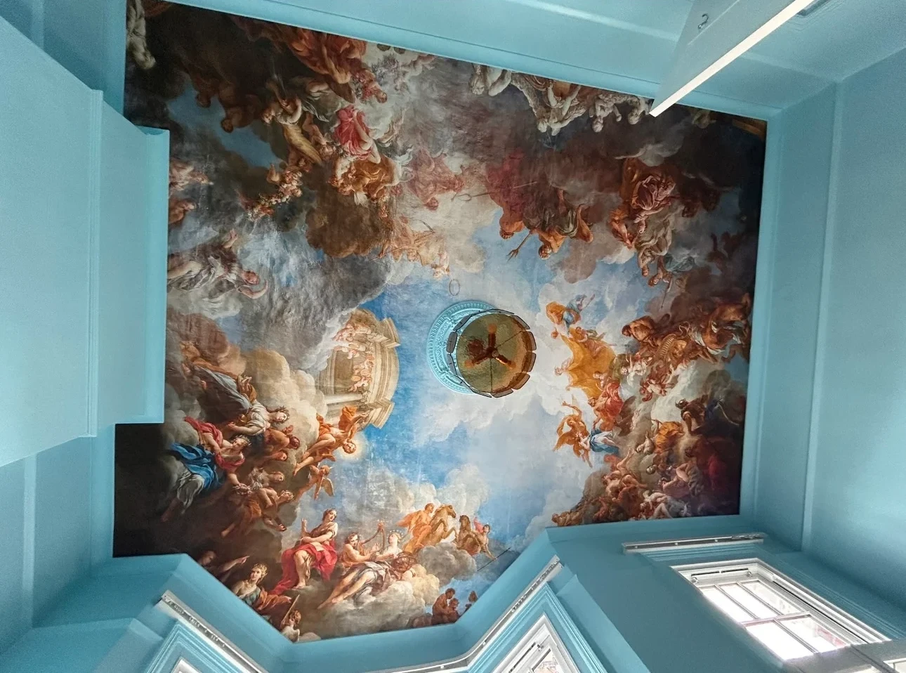 Ceiling hung with a classical sky mural wallpaper in a pale blue room