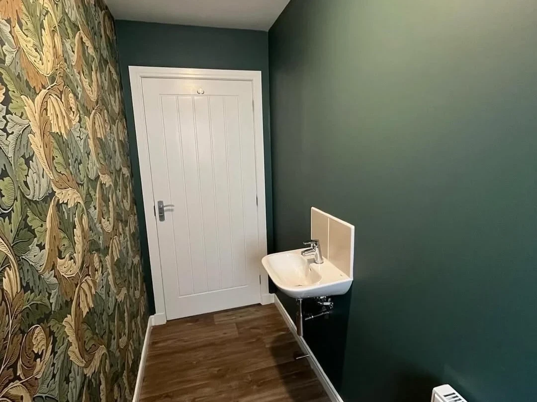 Cloakroom hung with bold botanical wallpaper beside dark green paintwork
