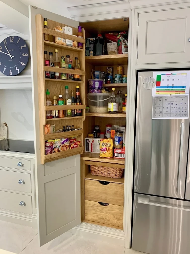 Painted larder cupboard with oak interior shelving beside a fridge